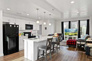 Kitchen with hanging light fixtures, black appliances, a kitchen island with sink, white cabinets, and sink