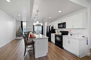 Kitchen with black appliances, pendant lighting, white cabinets, and a kitchen island with sink