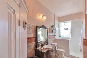 Bathroom with tile walls, toilet, vanity, and a textured ceiling