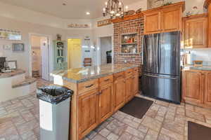 Kitchen featuring pendant lighting, backsplash, a chandelier, stainless steel refrigerator, and light stone counters