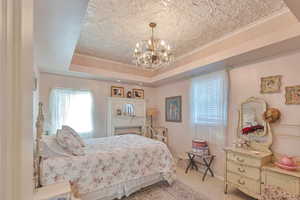 Carpeted bedroom with a raised ceiling, a notable chandelier, and crown molding