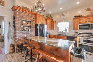 Kitchen featuring light stone countertops, a center island, stainless steel appliances, an inviting chandelier, and sink