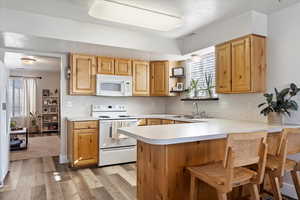 Kitchen featuring white appliances, sink, kitchen peninsula, light wood-type flooring, and a breakfast bar