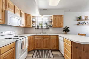 Kitchen with sink, white appliances, kitchen peninsula, and light wood-type flooring