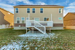 Snow covered rear of property with a wooden deck, a yard, and a patio