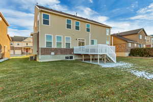 Back of house featuring a deck, a lawn, and central AC