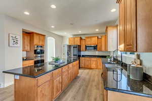 Kitchen with stainless steel appliances, dark stone counters, a kitchen island, light hardwood / wood-style flooring, and sink