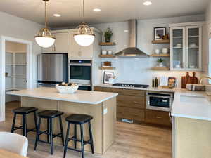 Kitchen with wall chimney exhaust hood, stainless steel appliances, sink, a kitchen breakfast bar, and light hardwood / wood-style flooring