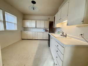 Kitchen with black dishwasher, white cabinetry, sink, and hanging light fixtures