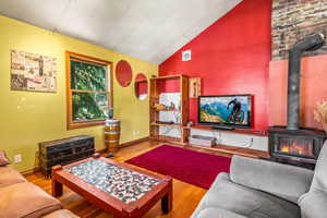 Living room featuring light hardwood / wood-style floors, a wood stove, and lofted ceiling