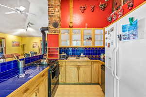 Kitchen featuring tile counters, backsplash, black stove, white refrigerator with ice dispenser, and sink