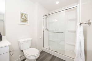 Bathroom with a shower with shower door, vanity, toilet, and hardwood / wood-style flooring