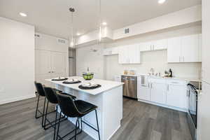 Kitchen with white cabinetry, appliances with stainless steel finishes, dark hardwood / wood-style flooring, hanging light fixtures, and a kitchen island