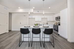 Kitchen with a center island, pendant lighting, hardwood / wood-style flooring, stainless steel appliances, and white cabinets