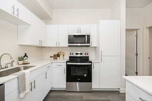 Kitchen with appliances with stainless steel finishes, dark hardwood / wood-style flooring, white cabinetry, and sink