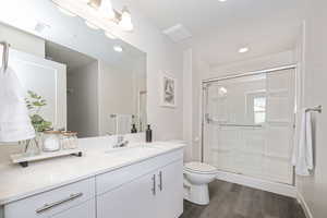 Bathroom with toilet, wood-type flooring, an enclosed shower, a textured ceiling, and vanity