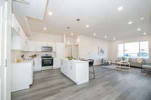 Kitchen with white cabinets, appliances with stainless steel finishes, a kitchen island, decorative light fixtures, and sink