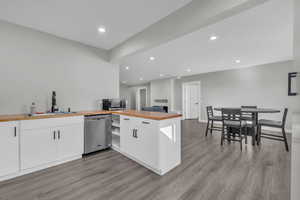 Kitchen with stainless steel dishwasher, white cabinets, wooden counters, and sink