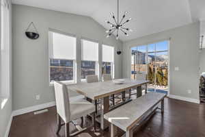 Dining room with dark wood-type flooring, vaulted ceiling, and an inviting chandelier