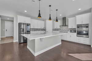 Kitchen with appliances with stainless steel finishes, wall chimney exhaust hood, and white cabinets