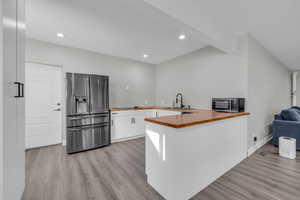 Kitchen featuring kitchen peninsula, sink, white cabinetry, light hardwood / wood-style flooring, and stainless steel fridge with ice dispenser