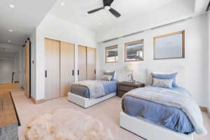 Carpeted bedroom featuring ceiling fan, a barn door, and two closets