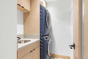 Laundry room featuring cabinets, stacked washer / drying machine, and sink