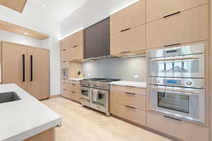 Kitchen with light brown cabinetry, appliances with stainless steel finishes, tasteful backsplash, and light wood-type flooring