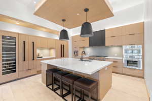 Kitchen featuring decorative light fixtures, sink, light brown cabinetry, and a kitchen island with sink