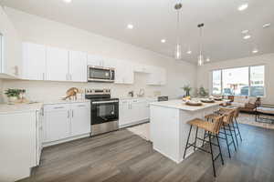 Kitchen with dark wood-type flooring, white cabinets, appliances with stainless steel finishes, and a kitchen island