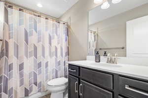 Bathroom with toilet, vanity, and curtained shower