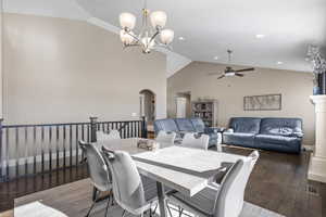 Dining area featuring ceiling fan with notable chandelier, dark hardwood / wood-style flooring, and vaulted ceiling