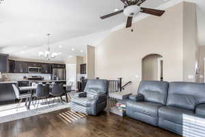 Living room with lofted ceiling, dark wood-type flooring, sink, and ceiling fan with notable chandelier