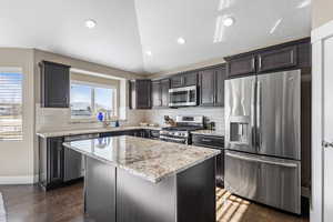 Kitchen featuring vaulted ceiling, a center island, sink, light stone countertops, and appliances with stainless steel finishes