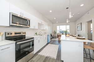 Kitchen featuring a kitchen island, a kitchen bar, white cabinetry, stainless steel appliances, and hanging light fixtures