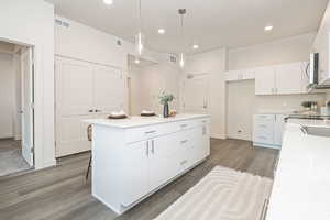 Kitchen with white cabinetry, dark hardwood / wood-style floors, a kitchen island, and decorative light fixtures