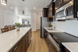 Kitchen with light hardwood / wood-style floors, stainless steel appliances, hanging light fixtures, dark brown cabinetry, and sink