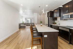 Kitchen with stainless steel appliances, decorative light fixtures, light wood-type flooring, a breakfast bar, and a center island