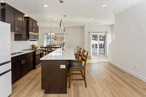 Kitchen with light hardwood / wood-style floors, hanging light fixtures, appliances with stainless steel finishes, and a center island