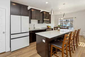 Kitchen featuring dark brown cabinetry, a kitchen island, light hardwood / wood-style floors, sink, and hanging light fixtures