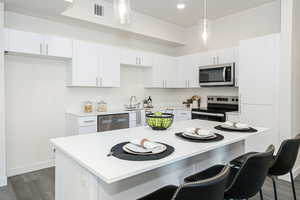 Kitchen with pendant lighting, appliances with stainless steel finishes, a kitchen island, dark wood-type flooring, and white cabinetry