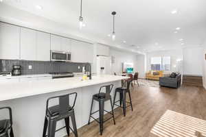 Kitchen featuring decorative light fixtures, white cabinetry, light hardwood / wood-style flooring, a kitchen breakfast bar, and stainless steel appliances