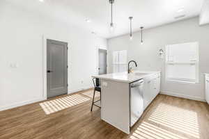 Kitchen featuring decorative light fixtures, stainless steel dishwasher, sink, light wood-type flooring, and white cabinets