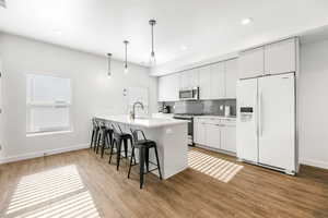 Kitchen featuring white cabinetry, appliances with stainless steel finishes, light wood-type flooring, hanging light fixtures, and sink