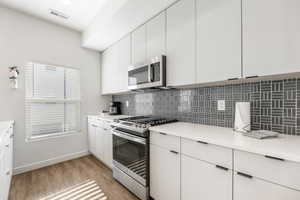 Kitchen with appliances with stainless steel finishes, decorative backsplash, light hardwood / wood-style flooring, and white cabinets