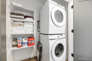 Laundry area with dark hardwood / wood-style flooring and stacked washing maching and dryer