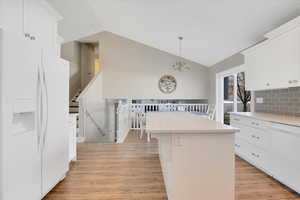 Kitchen with vaulted ceiling, a center island, decorative backsplash, white appliances, and white cabinetry