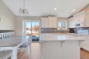 Kitchen with white appliances, pendant lighting, a kitchen island, white cabinetry, and an inviting chandelier