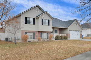 Split level home with a garage, a front yard, and central AC