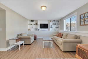 Living room with built in features and light hardwood / wood-style floors